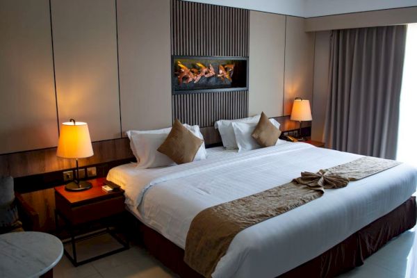 The image shows a neatly arranged hotel room with a large bed, bedside tables with lamps, and a decorative wall feature above the bed.