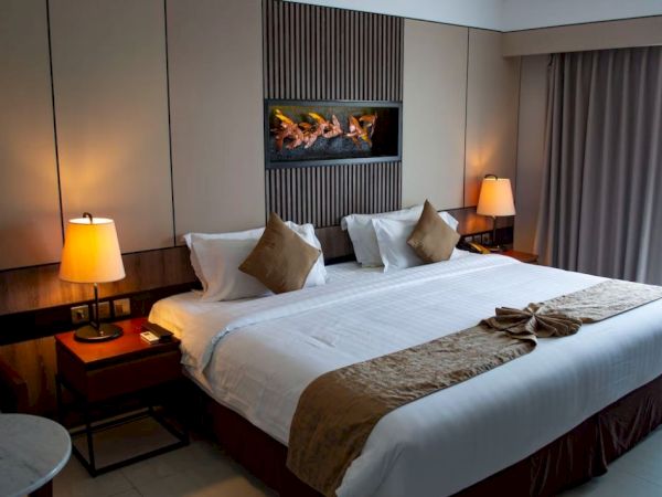 The image shows a neatly arranged hotel room with a large bed, bedside tables with lamps, and a decorative wall feature above the bed.