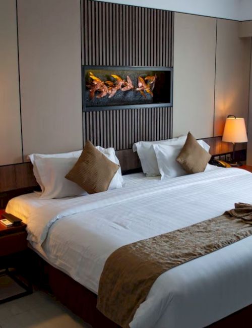 A hotel room with a large bed, pillows, decorative towels, side tables with lamps, and curtains covering a window.
