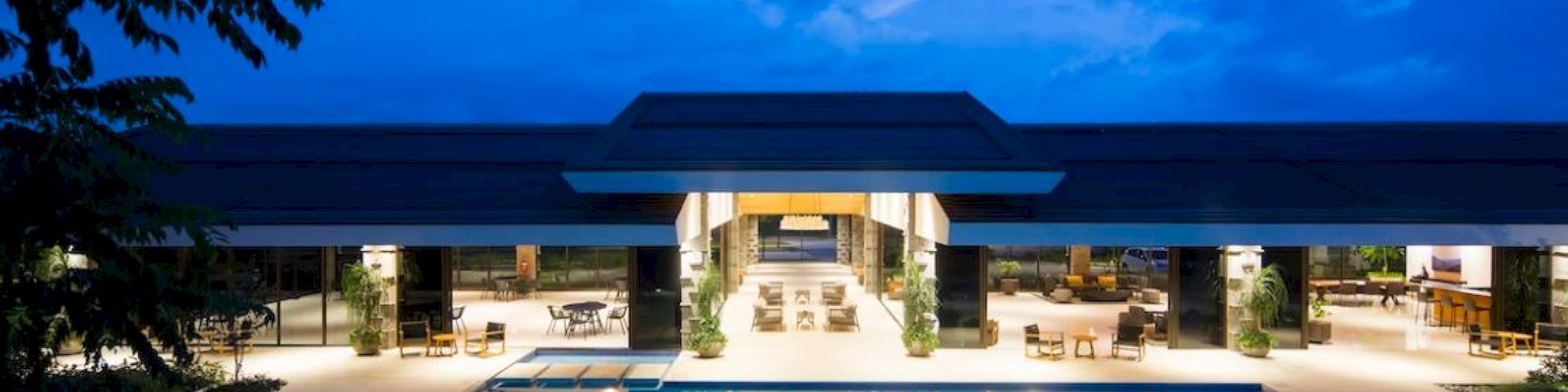 A luxurious modern building with an illuminated pool, seating areas, and a vibrant evening sky.