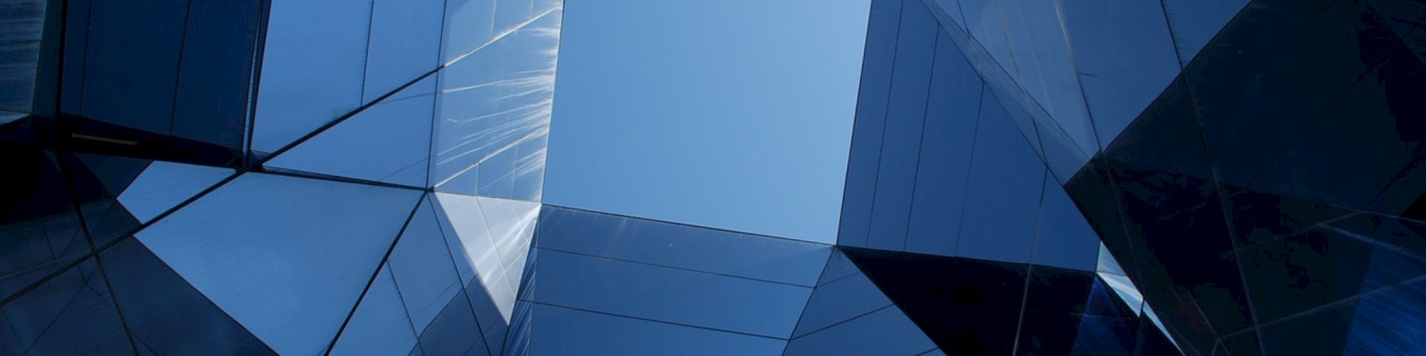 Geometric glass structures create a symmetrical pattern with a clear blue sky visible through the center.