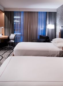 A modern hotel room with two beds, a large TV, desk area, and stylish decor featuring a patterned wall and curtains.