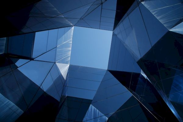 The image shows the sky framed by angular glass architectural structures reflecting light, creating a geometric and modern abstract effect.