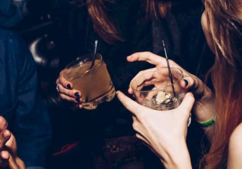 The image shows people socializing at a gathering, holding drinks and smiling.