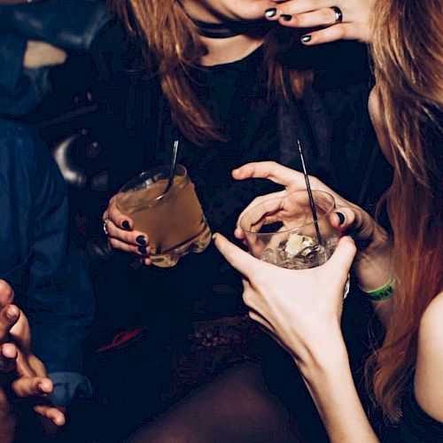 The image shows people socializing at a gathering, holding drinks and smiling.