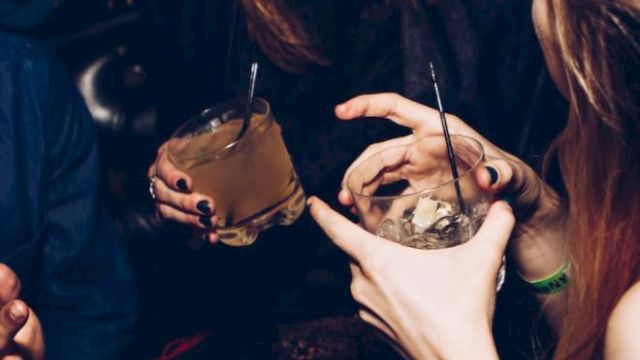The image shows people socializing at a gathering, holding drinks and smiling.