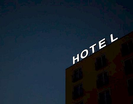 A building at night with a partially lit "HOTEL" sign, missing the letter "H," against a dark sky, creating a mysterious ambiance.