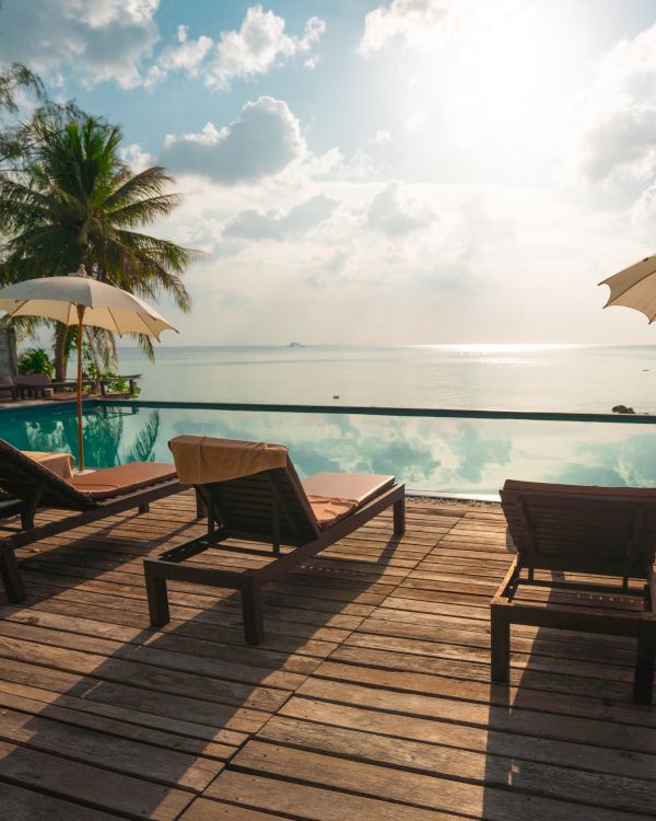 A picturesque tropical scene with lounge chairs, umbrellas, and a swimming pool overlooking a calm sea under a partly cloudy sky.