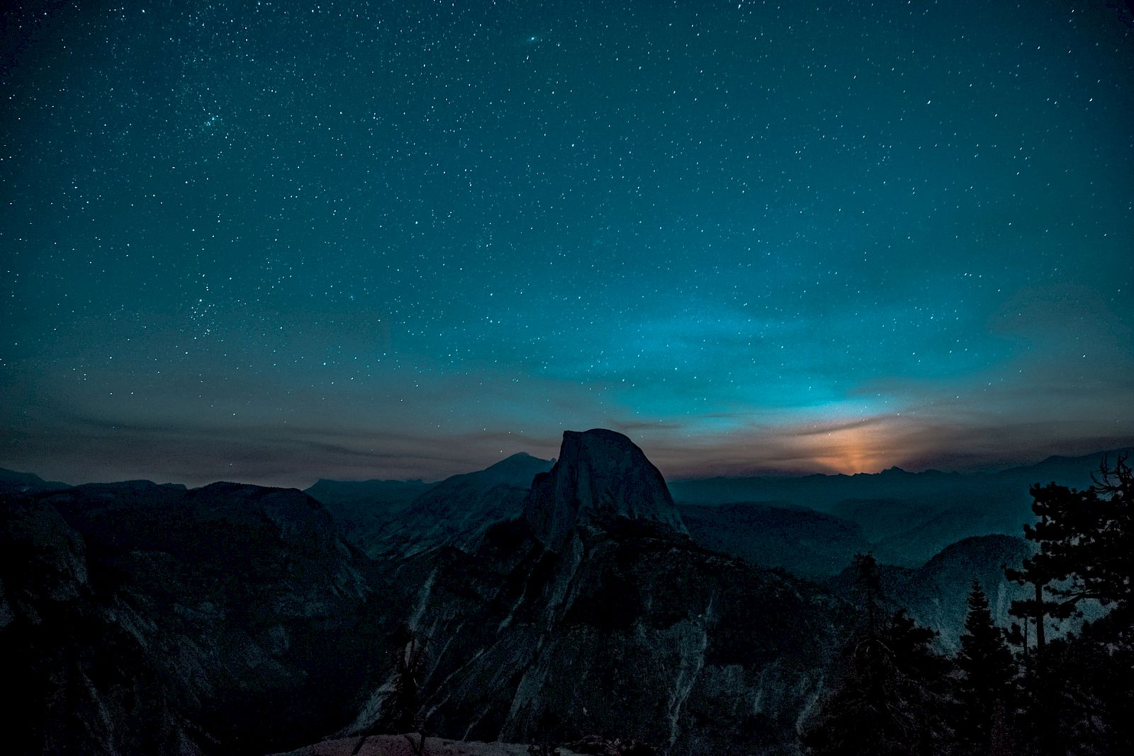A starry night sky over a mountain silhouette with a glowing moon peeking through, creating a serene, atmospheric scene.