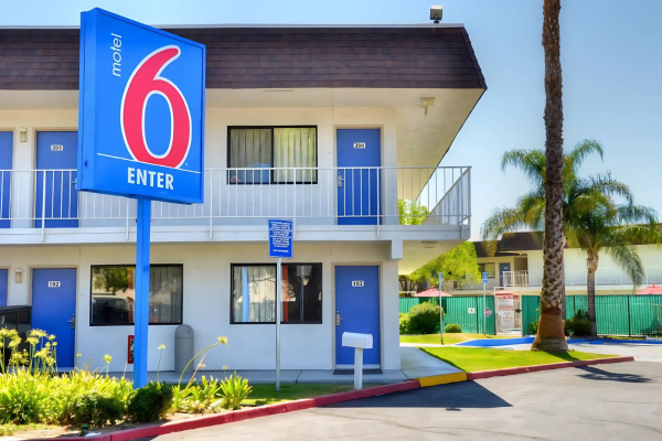 A two-story Motel 6 building with a blue sign, surrounded by palm trees and a parking area.