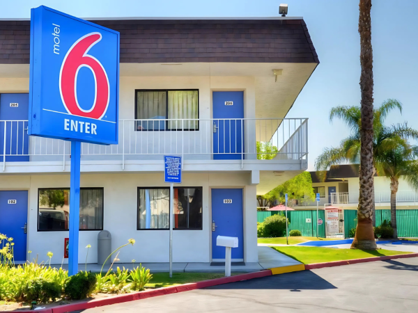 A two-story Motel 6 building with a blue sign, surrounded by palm trees and a parking area.