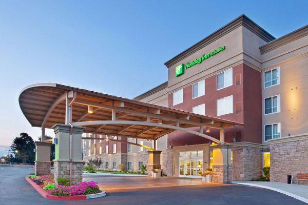 The image shows the exterior of a contemporary hotel building with a covered entrance and well-maintained landscaping.
