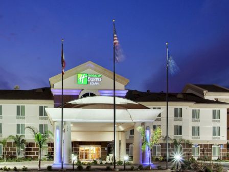 A hotel building at dusk with multi-story architecture, illuminated entrance, and three flagpoles in front.
