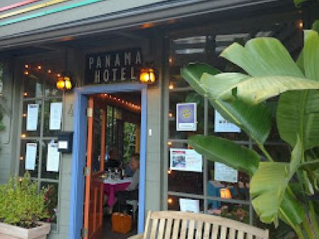 The image shows the entrance of the Panama Hotel with a bench and plants outside, featuring a colorful roof and various signs.