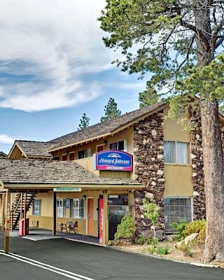 A two-story motel with a rustic facade surrounded by trees and a parking lot in front. The sign reads "Alpenrose Inn" near the entrance.