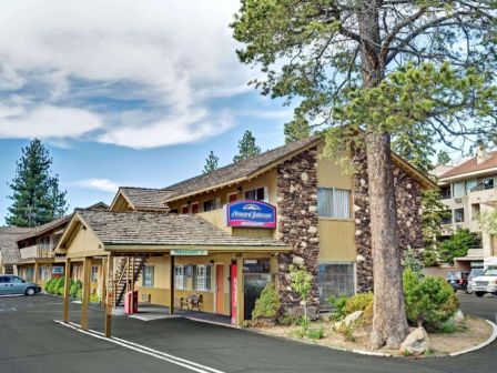 A two-story motel with a rustic facade surrounded by trees and a parking lot in front. The sign reads "Alpenrose Inn" near the entrance.