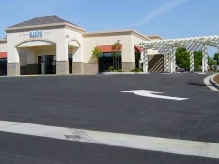 The image shows a bank building with a drive-through lane and an empty parking area under a clear blue sky.