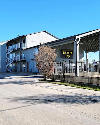 The image shows a three-story motel building with a sign that reads "Travel Inn," featuring outdoor corridors and a parking area.