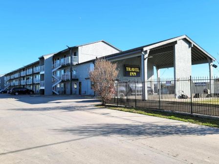 The image shows a three-story motel building with a sign that reads "Travel Inn," featuring outdoor corridors and a parking area.