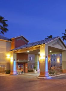 A brightly lit hotel entrance at dusk, surrounded by palm trees, with a clear evening sky in the background.
