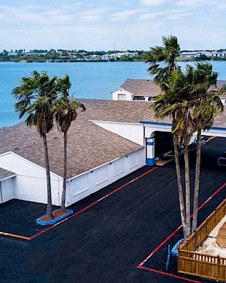 The image shows a Motel 6 near a body of water with palm trees and a pergola-covered area, captured on a sunny day.