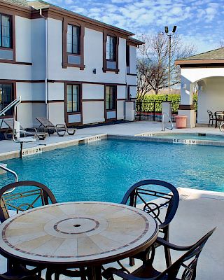An outdoor pool area with chairs and tables, adjacent to a two-story building under a clear sky.