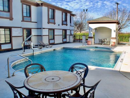 An outdoor pool area with chairs and tables, adjacent to a two-story building under a clear sky.