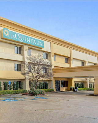 The image shows a La Quinta hotel building with a parking area, trees, and a clear, sunny sky above.