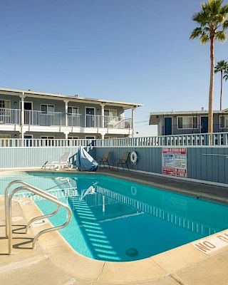 A fenced outdoor pool area in a sunny motel setting, with lounge chair and palm trees nearby.