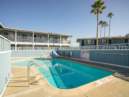 A fenced outdoor pool area in a sunny motel setting, with lounge chair and palm trees nearby.