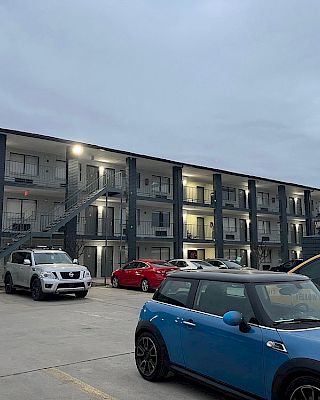 A three-story motel with external staircases and several parked cars. A bright red sign is visible on top of the building.
