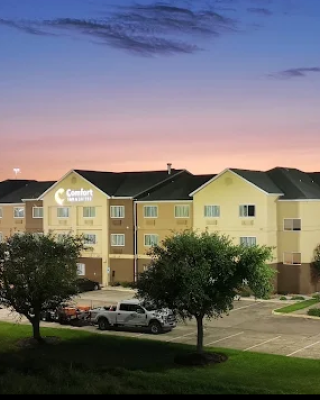 A hotel building with a "Comfort Suites" sign, surrounded by a parking lot and trees, at sunset.