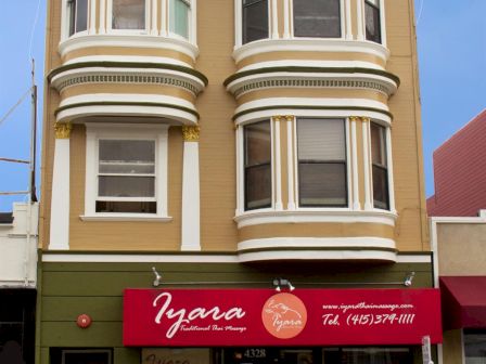 A three-story beige building with rounded bay windows and a red storefront sign reading &ldquo;Iyara&rdquo; on the ground floor.