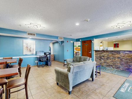 A welcoming hotel lobby with blue walls, a seating area of chairs and a sofa, a reception desk, and tables for guests.