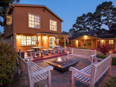 Cozy two-story house with a lit backyard patio, wooden benches around a fire pit, string lights, and shaded trees in the dusk.