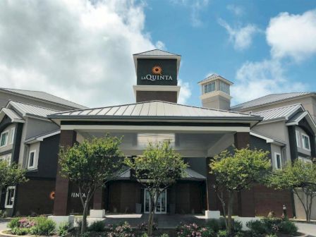 A La Quinta hotel exterior with a tall sign tower and landscaped entrance under a cloudy sky.