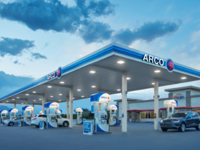 An ARCO gas station with multiple fuel pumps and a few cars under a blue sky with scattered clouds.