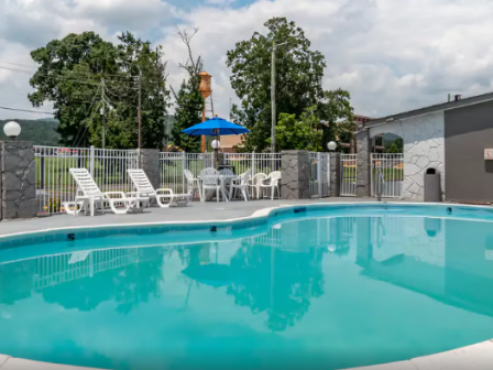 An outdoor swimming pool with blue water, white lounge chairs, a small umbrella, and fenced yards around it.