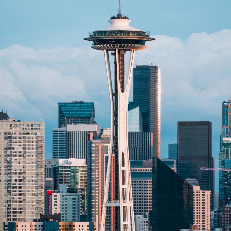 The image shows the Seattle Space Needle towering over the city's skyline with clouds in the background.