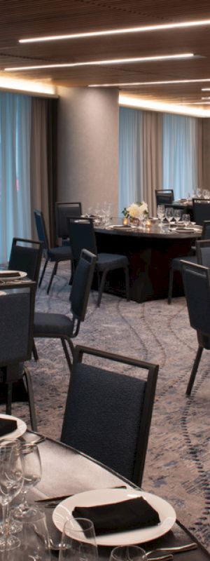 The image shows a banquet hall with round tables, elegantly set for an event, featuring blue chairs and soft lighting in a modern space.