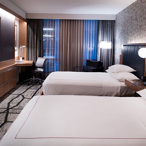 A modern hotel room with two double beds, a large TV, a desk, and contemporary decor.