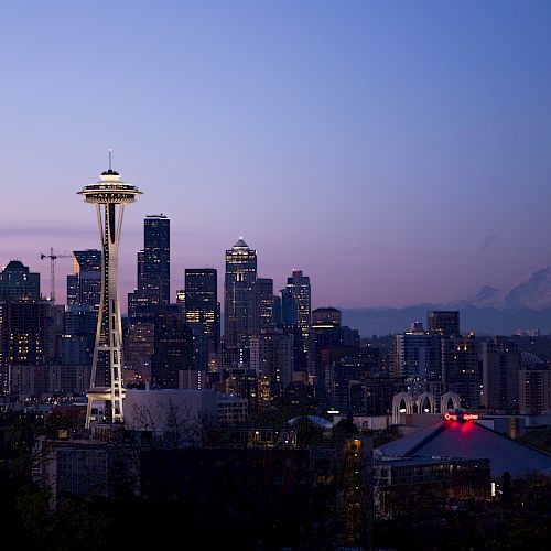 Seattle skyline at dusk with the Space Needle and Mount Rainier in the background under a clear sky.